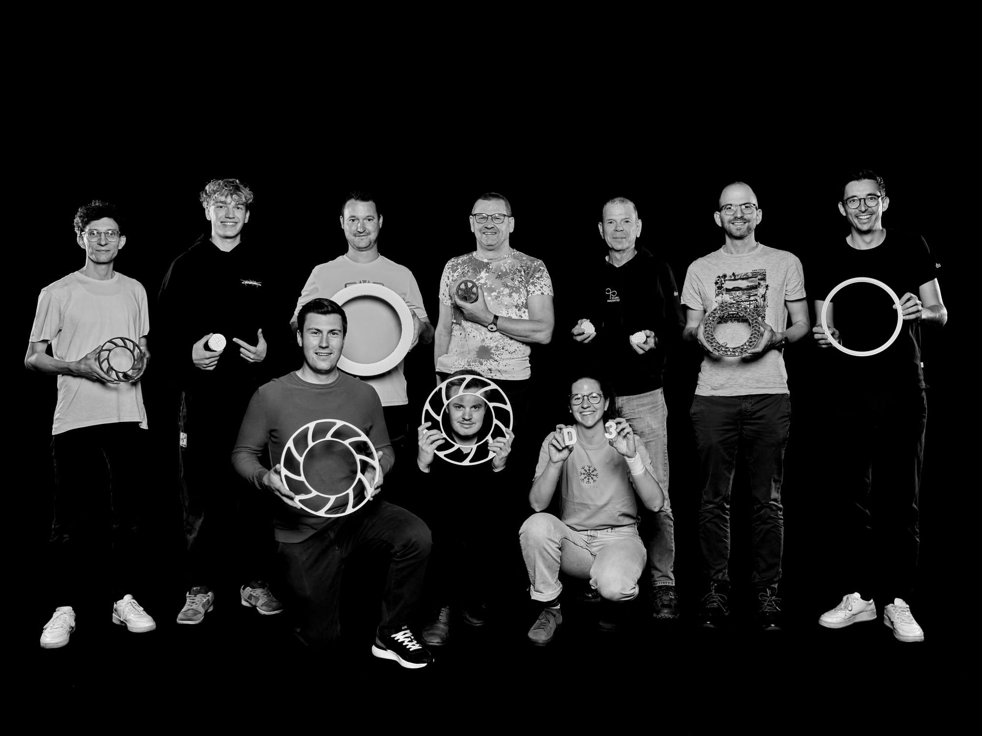 Ten members of the D3-AM team holding ceramic components against a black background