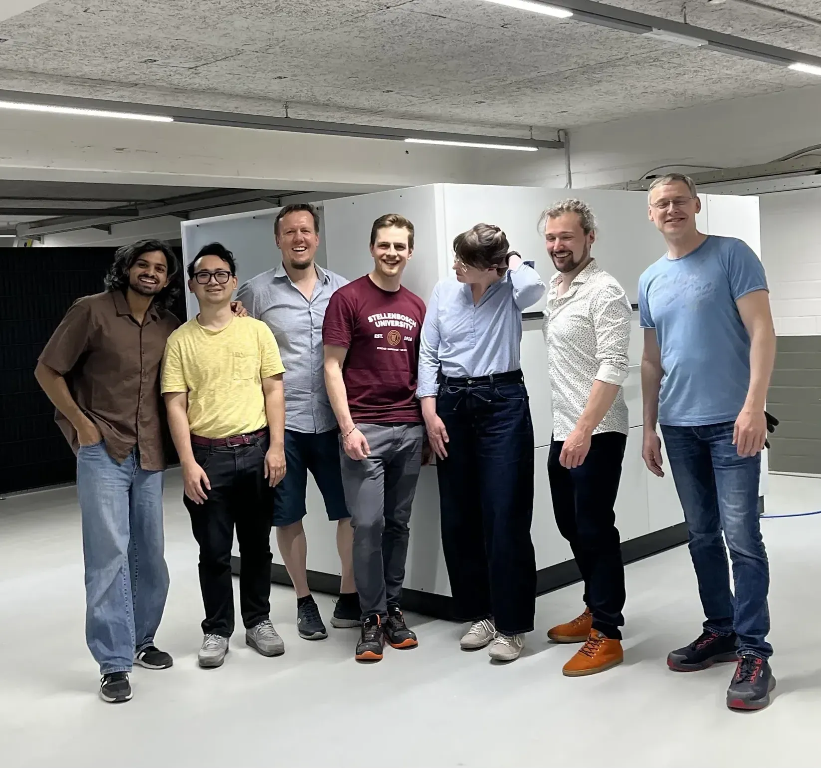 Seven members of the NUWAM team standing together in front of a machine in Radeberg